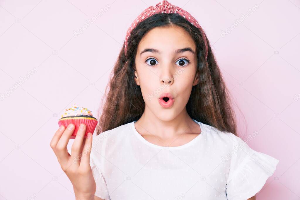 Cute hispanic child girl holding cupcake scared and amazed with open mouth for surprise, disbelief face 