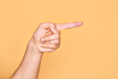 İzole edilmiş sarı arka plan üzerinde parmaklarını gösteren beyaz bir gencin eli işaret parmağıyla kenarı işaret ediyor ve bir seçim yapıyor.