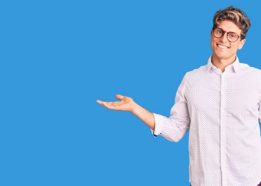 İş kıyafetleri ve gözlük takan genç yakışıklı adam gülümsüyor. İki elini de açık tutuyor. Karşılaştırma ve reklam karşılaştırması yapıyor ve dengeyi sağlıyor. 