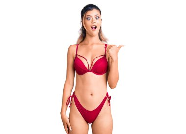 Bikini giyen genç ve güzel bir kadın elleri yana doğru işaret ederek şaşırdı, ağzı açık hayret içinde kaldı.. 