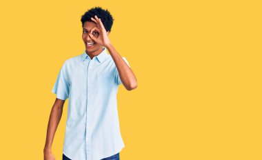 Genç Afro-Amerikan adam günlük kıyafetler giyiyor. El hareketleriyle gülümsüyor, gözleriyle mutlu yüzle parmaklarının arasından bakıyor.. 