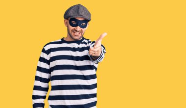 Hırsız maskesi takan genç yakışıklı adam dostça bir selamlama ve hoş geldin hediyesi olarak el sıkışmayı sunuyor. başarılı iş. 