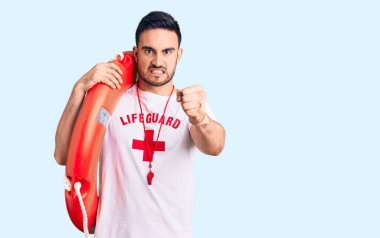 Cankurtaran üniforması giyen genç yakışıklı adam kızmış ve sinirlenmiş bir şekilde süzülüyor, öfkeyle bağırıyor ve el kaldırıyor. 