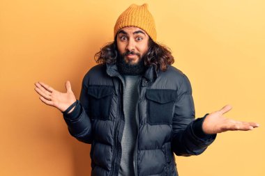 Sıradan kışlık giysiler giyen genç bir Arap, elleri ve kolları havada, kafası karışık bir ifade takınıyor. şüphe kavramı. 