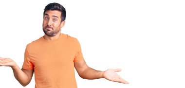 Sıradan kıyafetler giyen, elleri ve kolları havada, kafası karışmış genç İspanyol bir adam. şüphe kavramı. 