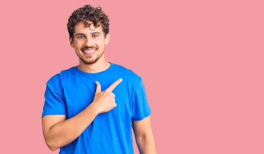 Kıvırcık saçlı, neşeli giyinen, yüzünde gülücükler açan, mutlu ve doğal bir ifadeyle elini ve parmağını kaldıran genç yakışıklı bir adam. 