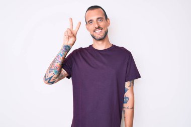 Dövmeli genç ve yakışıklı bir adam. Günlük giysiler giyiyor. İki numarayı gösterip işaret ediyor.. 