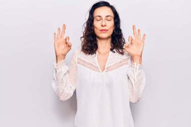 Genç ve güzel İspanyol kadın günlük kıyafetler giyip rahatlıyor ve gözleri kapalı gülümsüyor parmaklarıyla meditasyon hareketi yapıyor. yoga konsepti. 