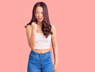 Genç, güzel Çinli bir kız, rahat kıyafetler giyiyor kızgın ve kızgın yumruğunu kaldırıyor ve öfkeyle bağırıyor. öfke ve agresif konsept. 