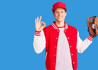 Beyzbol üniforması giyen yakışıklı genç adam elinde Golve ve topu tutarak tamam işareti yapıyor, gülümseyerek mükemmel bir sembol oluşturuyor. 