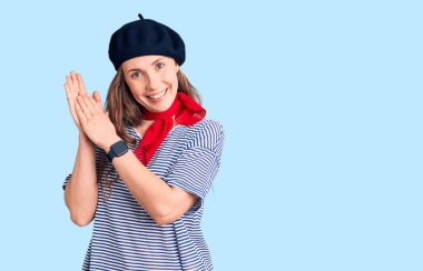 Fransız beresi ve çizgili tişört giyen genç ve güzel sarışın kadın alkışlıyor ve mutlu ve neşeli, gururlu elleri birlikte alkışlıyor. 