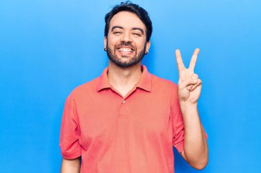 Gündelik kıyafetler giyen, gülümseyen ve kameraya göz kırpan genç İspanyol adam zafer işareti yapıyor. İki numara.. 