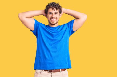 Kıvırcık saçlı, rahat giyinen, esneyen, kolları ve elleri başının arkasında olan, mutlu gülümseyen yakışıklı bir adam. 