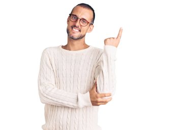 Gündelik kıyafetler ve gözlük takan, yüzünde kocaman bir gülümseme olan, eli ve parmağı kameraya bakan genç yakışıklı bir adam.. 