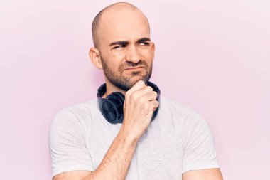 Genç yakışıklı kel adam müzik dinliyor. Kulaklık kullanıyor. Kuşkuya odaklanmış düşünüyor. 