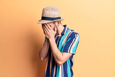 Sakallı, yaz şapkalı ve tişörtlü, suratını ellerle kapatıp ağlayan yakışıklı bir genç. depresyon kavramı. 