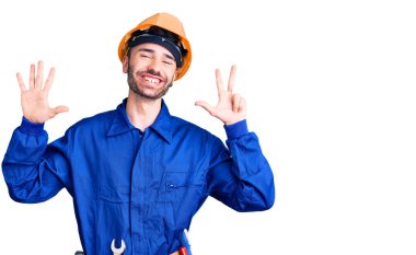 İşçi üniforması giyen genç İspanyol adam sekiz numarayı gösterip işaret ederken kendinden emin ve mutlu gülümsüyor.. 