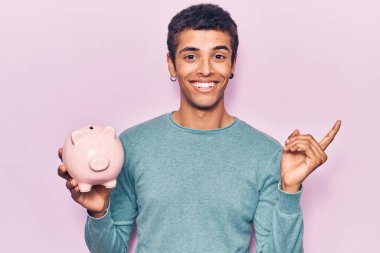 Genç Afrikalı Amerikalı domuz kumbarası tutan adam gülümsüyor. 