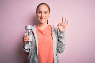 Genç, güzel, sportif bir kadın ferahlatıcı su şişesi içiyor. Parmaklarıyla imza atıyor. Mükemmel bir sembol.
