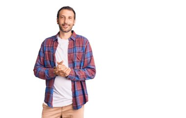 Elleri çapraz parmaklı, rahat ve neşeli gülümseyen sıradan kıyafetler giyen genç yakışıklı bir adam. Başarı ve iyimserlik 