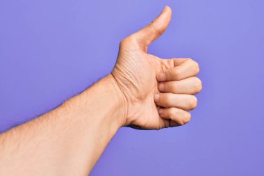 İzole edilmiş mor arka planda parmaklarını gösteren beyaz bir gencin eli başarılı bir onay jesti yapıyor. Başparmaklar yukarı, onaylama ve pozitif sembol ile.