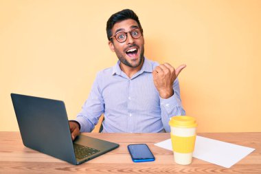 Ofiste çalışan, bir fincan kahve içen, ağzı açık gülümseyen genç bir İspanyol. 