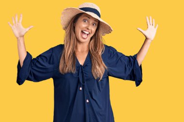 Orta yaşlı İspanyol kadın yaz şapkası takıyor ve parmaklarını onuncu parmaklarıyla gösterirken kendinden emin ve mutlu bir şekilde gülümsüyor.. 