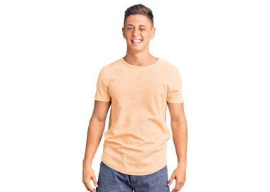 Gündelik kıyafetler giyen genç yakışıklı adam kameraya seksi bir ifadeyle bakıyor, neşeli ve mutlu bir yüzle.. 