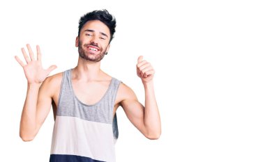 Latin asıllı genç adam gündelik giysiler giyip altı numaralı parmaklarıyla işaret ederken kendinden emin ve mutlu bir şekilde gülümsüyor.. 