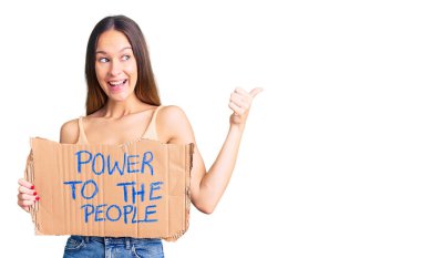 Güzel, esmer, genç bir kadın, insanların gücünü elinde tutuyor. Başparmağıyla yan tarafa işaret ediyor, ağzı açık gülümsüyor. 