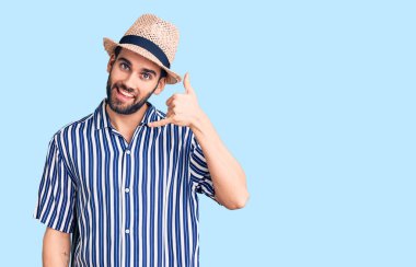 Sakallı, yaz şapkalı, çizgili tişörtlü, gülümseyen, el ve parmaklarıyla telefonla konuşan genç yakışıklı bir adam. iletişim kavramları. 