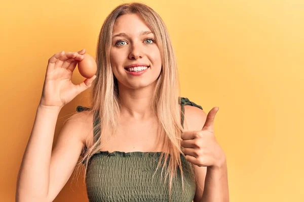 Mladá Blondýna Žena Drží Vejce Úsměvem Šťastný Pozitivní Palec Nahoru — Stock fotografie