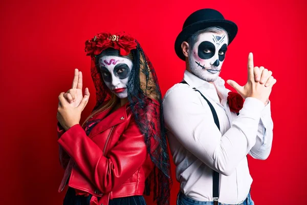 Couple wearing day of the dead costume over red holding symbolic gun with hand gesture, playing killing shooting weapons, angry face