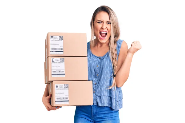 Jovem Mulher Loira Bonita Segurando Caixas Entrega Gritando Orgulhoso Celebrando — Fotografia de Stock