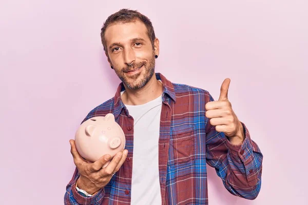 Young Handsome Man Holding Piggy Bank Smiling Happy Positive Thumb — Stock Photo, Image