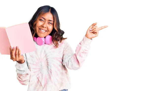 Joven Hermosa Mujer Raza Mixta Leyendo Libro Con Auriculares Sonriendo — Foto de Stock