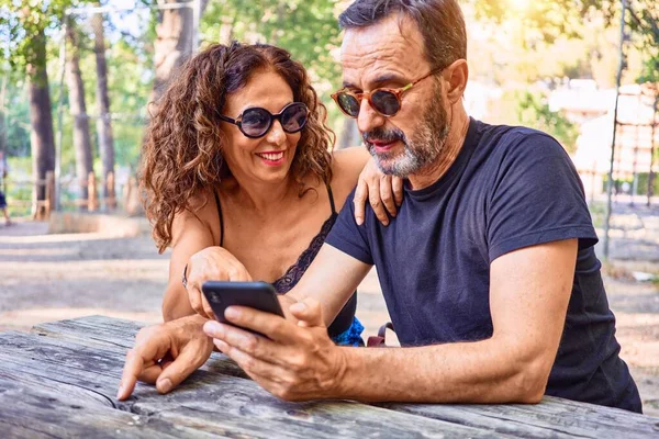 Medelålders Par Ler Glada Med Hjälp Smartphone Sitter Bänken Parken — Stockfoto