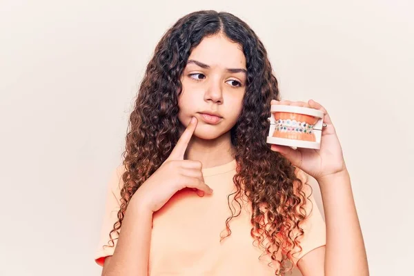 Beautiful Kid Girl Curly Hair Holding Orthodontic Serious Face Thinking — Stock Photo, Image