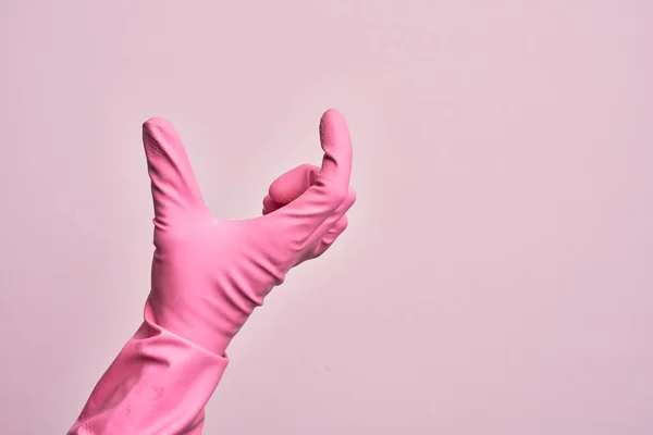 Hand of caucasian young man with cleaning glove over isolated pink background picking and taking invisible thing, holding object with fingers showing space