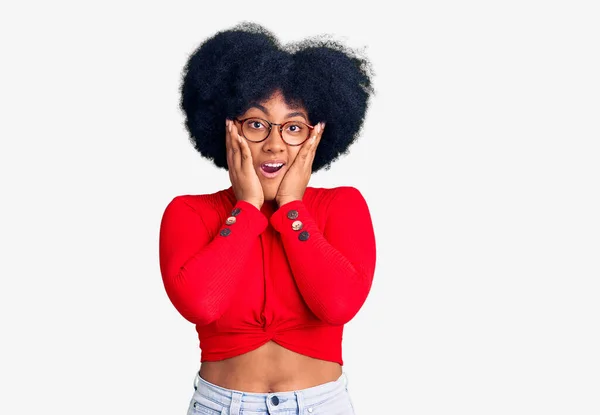 Young african american girl wearing casual clothes and glasses afraid and shocked, surprise and amazed expression with hands on face