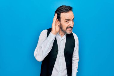 Soyutlanmış mavi arka plan üzerinde zarif gömlek ve yelek giyen yakışıklı bir adam kulağına fısıldayarak dedikodu ya da dedikoduları dinliyor. Sağırlık kavramı.