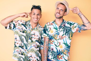 Yaz şapkası ve Hawaii tişörtü giyen iki genç eşcinsel adam tek parmakla kafaya doğru gülümsüyor, harika bir fikir ya da düşünce, iyi bir hafıza. 