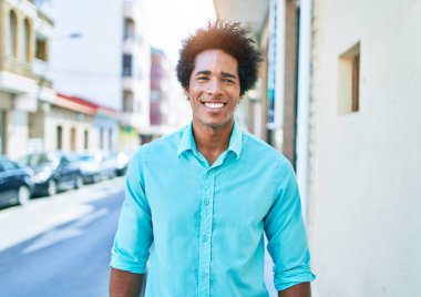 Genç, yakışıklı, Afro-Amerikan bir adam günlük giysiler giyip mutlu gülümsüyor. Yüzünde gülümsemeyle kasaba caddesinde yürürken.