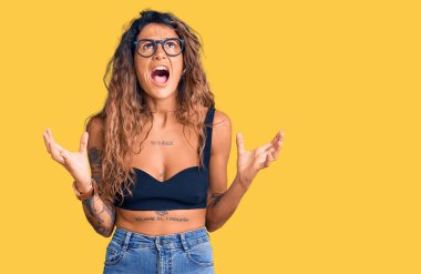 Gündelik kıyafetler ve gözlük takan Latin kökenli genç bir kadın deli gibi bağırıyor ve agresif bir ifadeyle bağırıyor ve kollarını kaldırıyor. hüsran kavramı. 