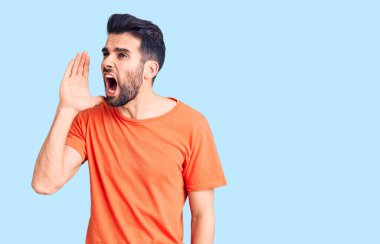 Sakallı, sıradan tişörtlü genç ve yakışıklı bir adam el pençe divan durup bağırıyor. iletişim konsepti. 