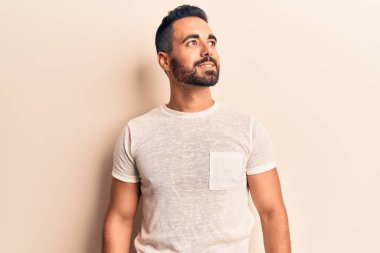 Latin kökenli genç bir adam günlük giysiler giyiyor, rahat bir görünüm takınıyor, doğal bir yüz ifadesi ve kendinden emin bir gülümsemeyle poz veriyor.. 