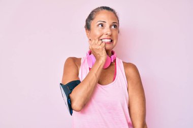 Orta yaşlı İspanyol kadın spor kıyafetleri giyiyor ve kulaklık takıyor. Ağzı tırnak yiyen eller yüzünden gergin ve stresli görünüyor. anksiyete. 
