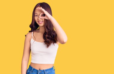 Genç, güzel Çinli kız günlük kıyafetler giyiyor. El hareketleriyle gülümsüyor, gözleriyle mutlu yüzle parmaklarının arasından bakıyor.. 