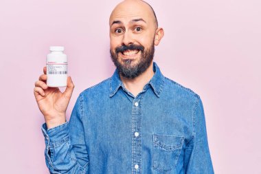 Elinde haplar tutan genç yakışıklı adam pozitif ve mutlu görünüyor. Durup gülümsüyor ve kendine güvenen bir gülümsemeyle dişlerini gösteriyor. 