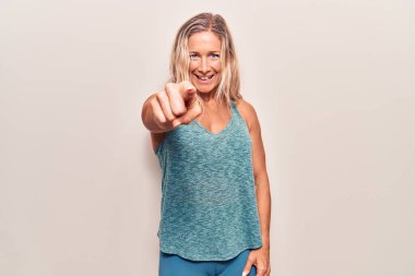 Orta yaşlı, beyaz giysili, spor kıyafetli bir kadın kameraya kızgın ve sinirli bir şekilde bakıyor. 